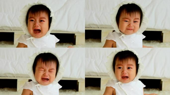 可爱甜美可爱的亚洲宝宝穿着白色连衣裙躺在白色床上哭泣，在舒适的卧室里情绪低落，健康的宝宝概念
