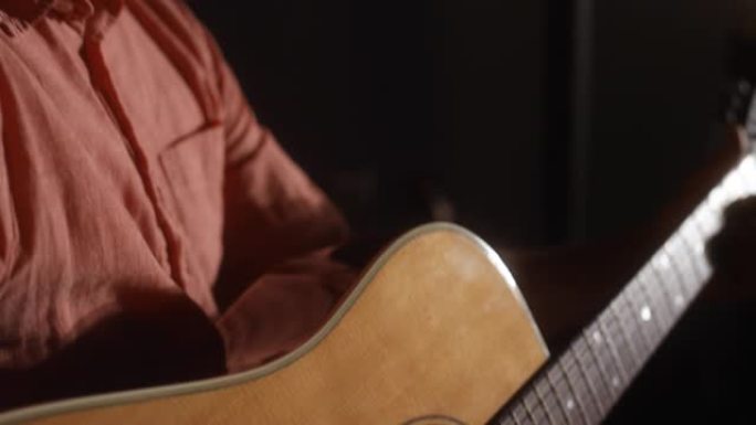 一名拉丁裔男性的特写镜头，向他平移，在昏暗的空间里弹吉他