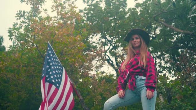一个戴牛仔帽、穿格子衬衫的女孩站着。背景是一面美国国旗在风中飘扬。