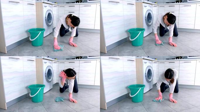 穿着粉红色橡胶手套的疲倦女人用布洗厨房地板。地板上的灰色瓷砖。