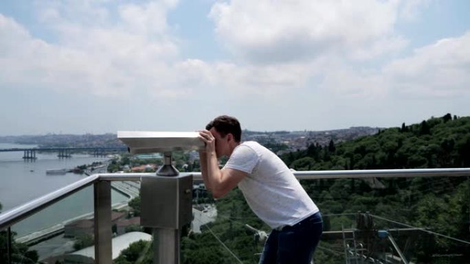 男子站在观景台上透过双筒望远镜看