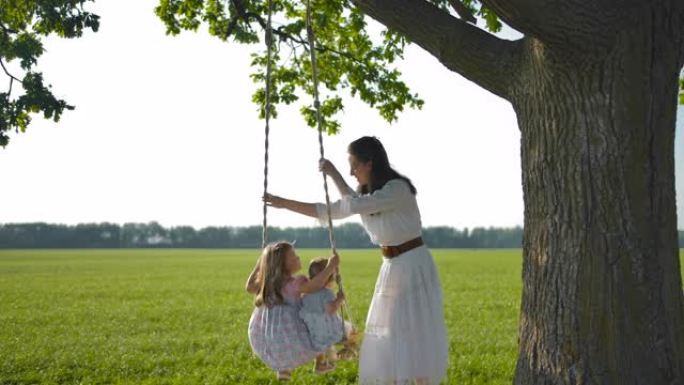 母亲在绑在一棵老橡树上的木绳秋千上摇晃女儿
