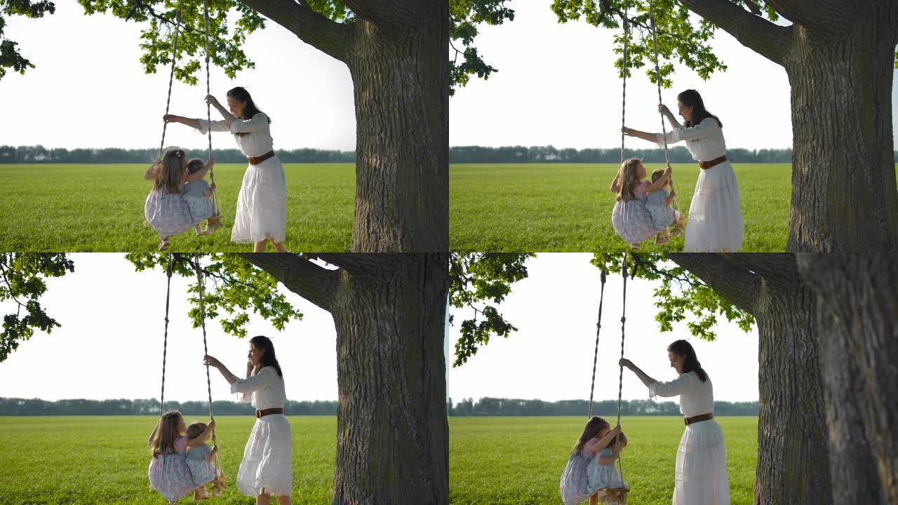 母亲在绑在一棵老橡树上的木绳秋千上摇晃女儿
