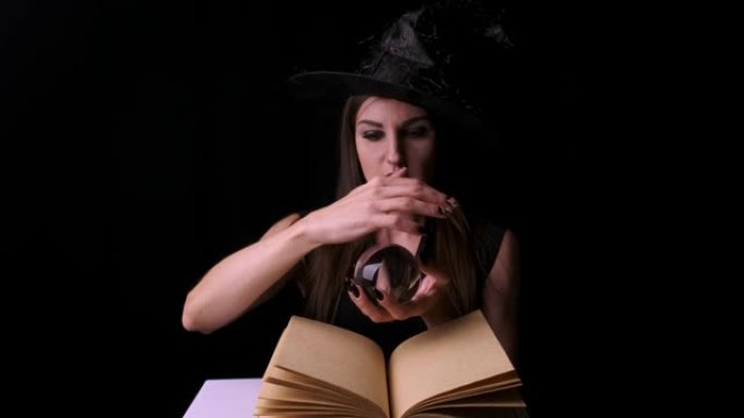 穿着黑色女巫服装和帽子的美女，手里拿着一个透明的魔球，让人联想。万圣节节日派对