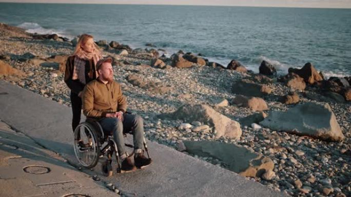 年轻女子正在护理生病的残疾男子，在海边滚动婴儿车
