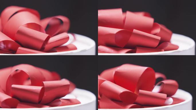黑色背景特写上有红色蝴蝶结旋转的白色礼品盒。