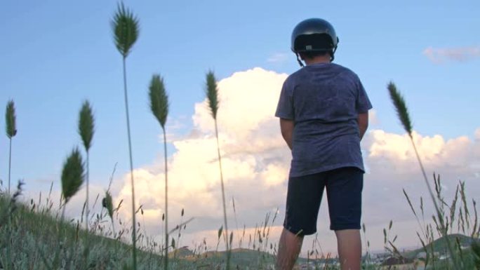 一个戴着头盔的男孩站在山上，看着夕阳下有村庄的山谷
