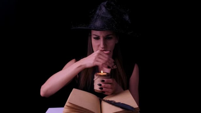 迷人的女巫，在黑色背景上，手里拿着一支蜡烛在一本咒语书上