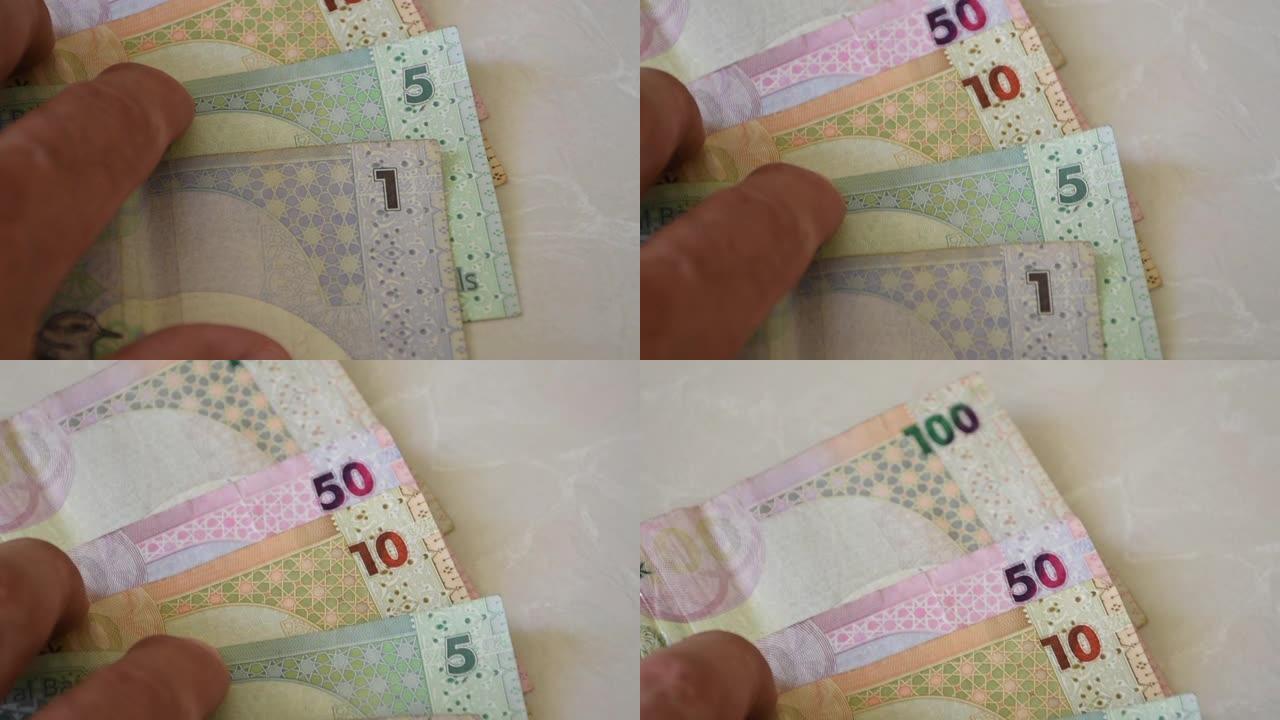 一只手伸出来散开卡塔尔的现钞，这种货币被称为卡塔尔里亚尔现钞，散布在白色背景上。货币兑换。