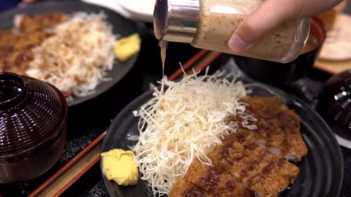 男人倒入沙拉酱和猪肉炸猪排 (由面包屑组成的日本菜)。