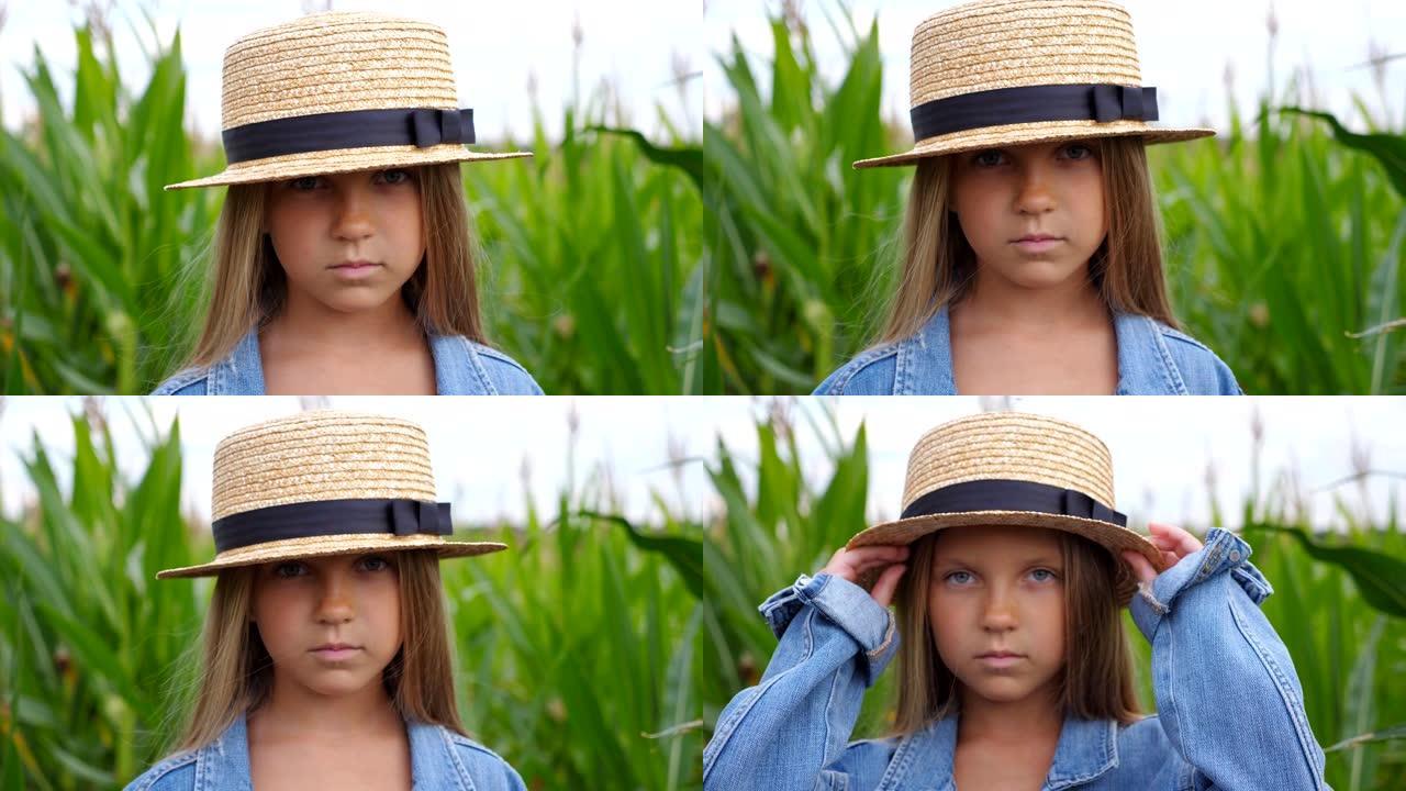 戴着草帽的小严肃女孩的肖像在有机农场玉米地模糊的背景下看着相机。小孩子站在草地上，拉直她长长的金发。
