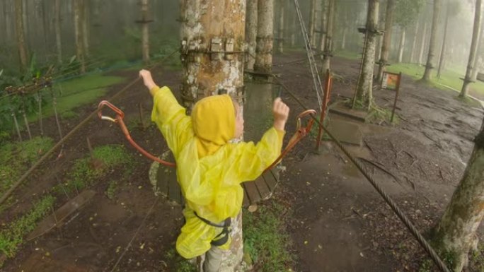 一个穿着安全带的小男孩在森林冒险公园的树梢上的路线上攀登的动作相机镜头。他爬上高高的绳索小径。带登山