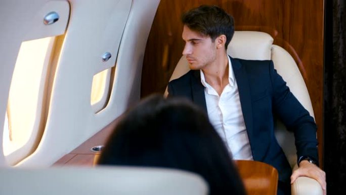 穿着西装的年轻商人坐在头等舱飞机上。穿着西装的可敬的富人乘坐私人飞机飞进去。