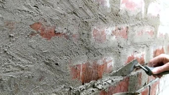 女人用砂浆指着砖墙。双手合拢。