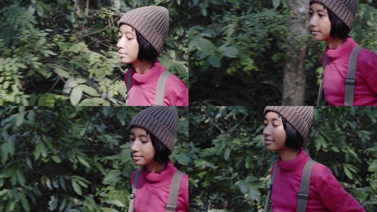 亚洲小女孩穿着长袖衬衫和羊毛帽子，一边散步，一边欣赏冬天的森林早晨的大自然。