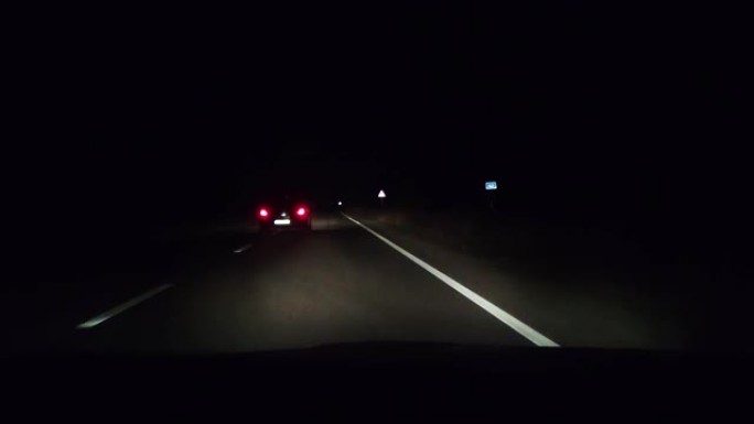 在夜间轨道上从出租车上观看。大灯照亮了汽车前面的沥青。迎面而来的车辆的前灯有时是可见的。在黑暗中安全