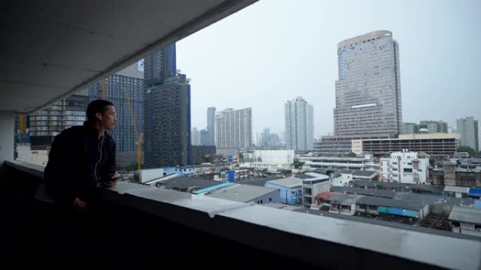 年轻的亚洲男子在泰国曼谷的城市backgground使用智能手机雨。