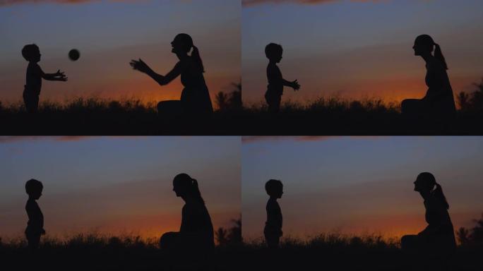 日落时，母亲和孩子在公园玩接球的剪影。