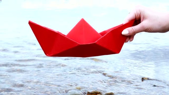 女人的手握着红色的纸船在河上