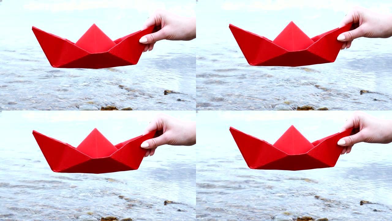 女人的手握着红色的纸船在河上