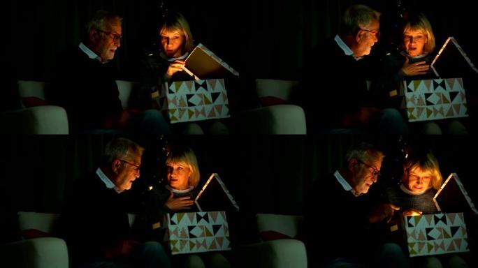 微笑的老年夫妇在圣诞节打开一个带有闪亮爆炸光线的礼品盒的慢动作镜头