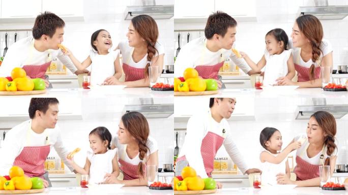4k慢动作，年轻的亚洲父亲母亲和女儿快乐而有趣地果酱在面包上，并在现代白色厨房里喂给父母。