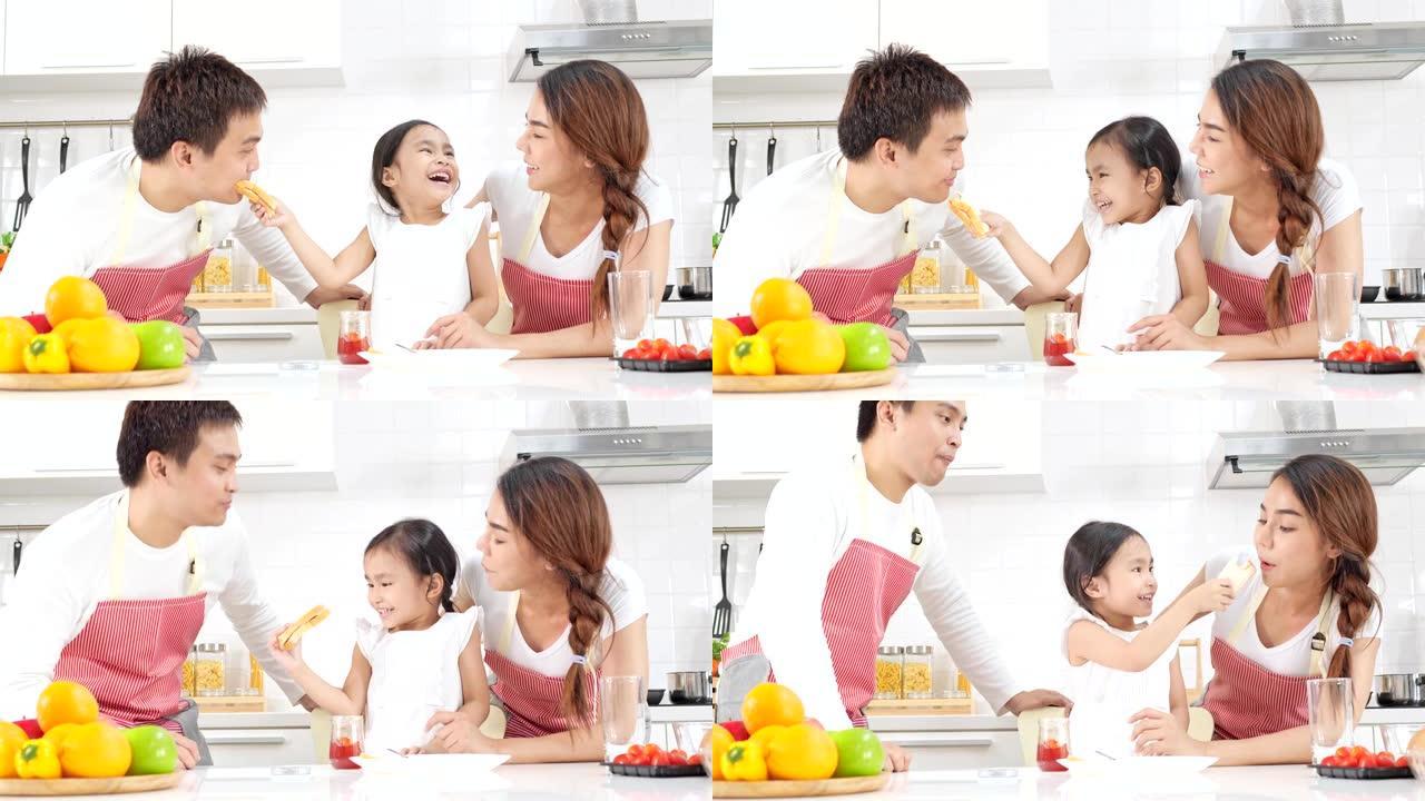 4k慢动作，年轻的亚洲父亲母亲和女儿快乐而有趣地果酱在面包上，并在现代白色厨房里喂给父母。