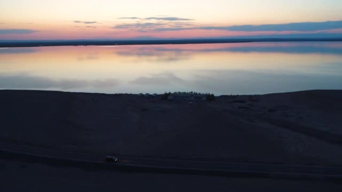 日落时在沙漠中部空旷的道路上行驶的汽车的鸟瞰图