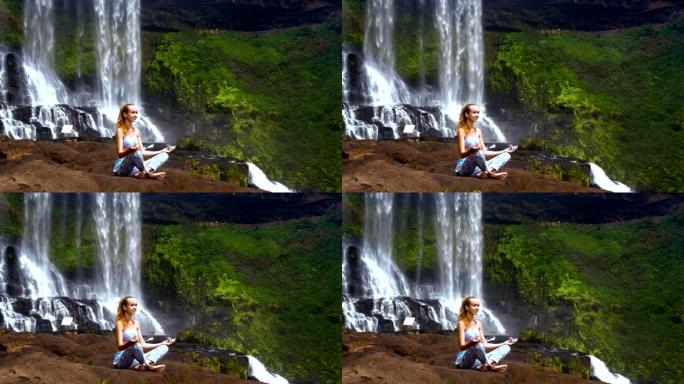女孩在瀑布的大石头上摆着调息瑜伽姿势