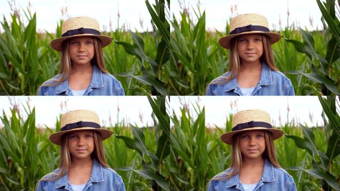 快乐的小孩的肖像，长长的金发站在玉米田模糊的背景下。戴着草帽的微笑小女孩在有机农场的草地上看着相机。