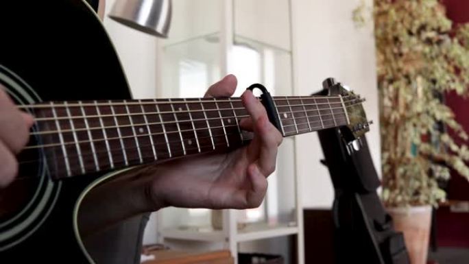 一个男人弹原声吉他的特写镜头。第6个品格上带有capo的手指采摘技术。