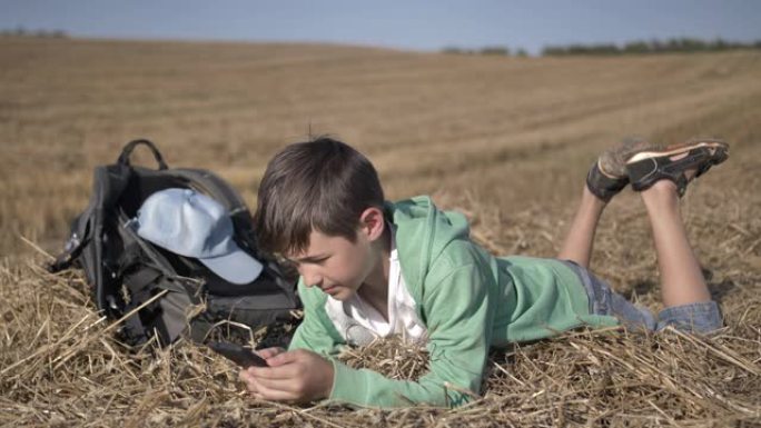 疲惫的男孩躺在田野里，在户外使用手机