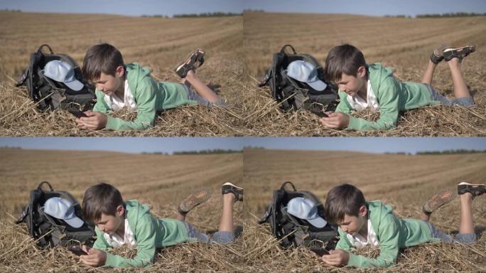疲惫的男孩躺在田野里，在户外使用手机
