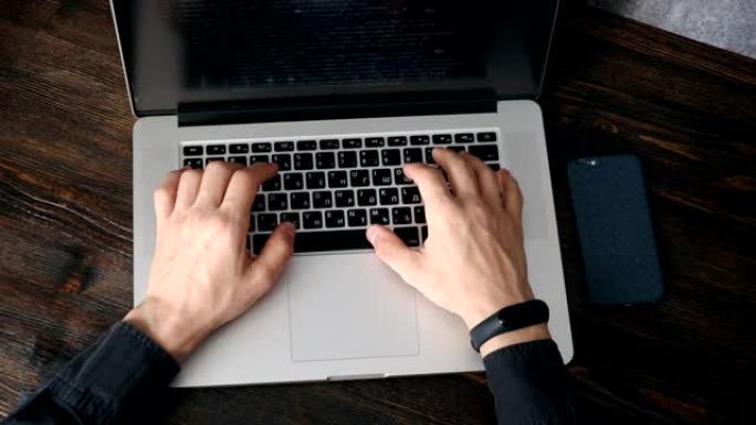 一位穿着黑色衬衫的男性程序员正在笔记本电脑上工作，程序代码和开发人员的手放在笔记本电脑上。现代年轻程