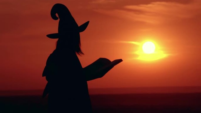 穿着化装和帽子的女孩女巫拿着日出的书