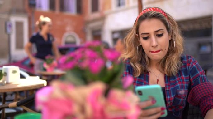 美国复古风格的女孩，红唇坐在当地咖啡馆附近，环顾四周。使用智能手机和发送信息的年轻模特。酒吧里迷人的