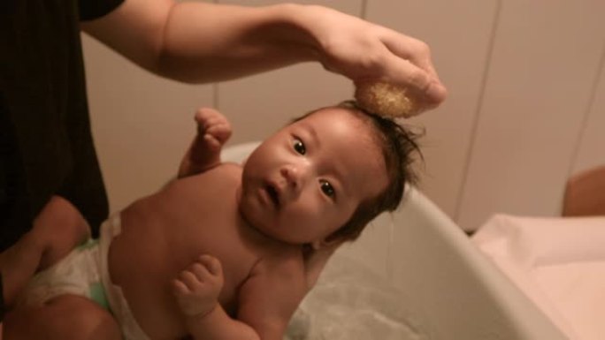 亚洲婴儿洗澡爸爸的胳膊。在家洗头发，温暖的光线，白天