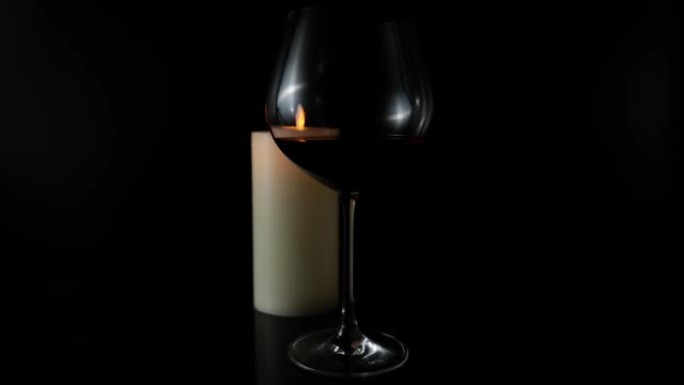 黑色背景上的一杯葡萄酒和一支燃烧的蜡烛。