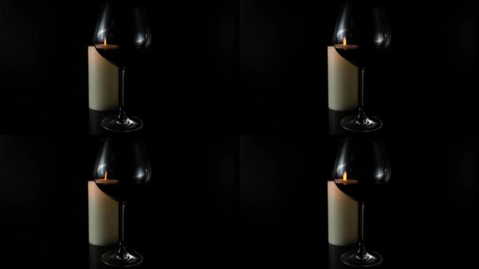 黑色背景上的一杯葡萄酒和一支燃烧的蜡烛。