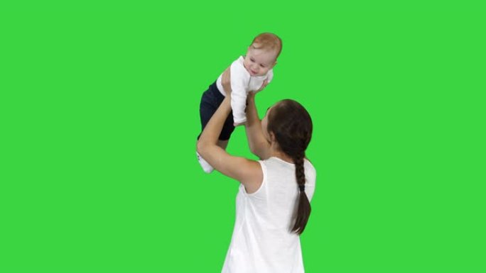 年轻的妈妈通过在绿色屏幕上抬起婴儿来玩婴儿，色度键