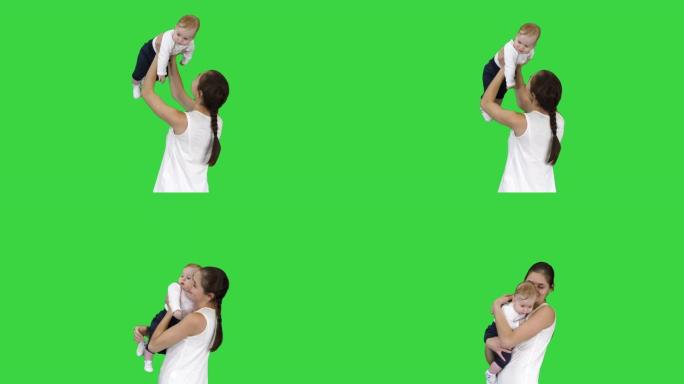 年轻的妈妈通过在绿色屏幕上抬起婴儿来玩婴儿，色度键