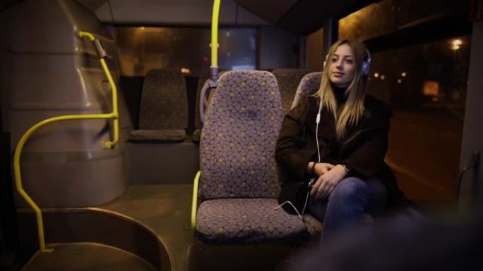 晚上乘公共汽车旅行时听音乐的女乘客。晚上，女孩在窗户旁边的行驶车辆上听音乐