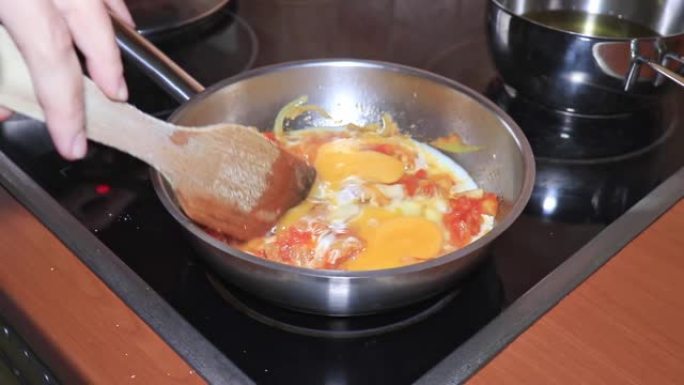 厨师在锅中煮煎蛋卷，在锅中切碎的西红柿和洋葱，在家里用蔬菜煮煎蛋卷