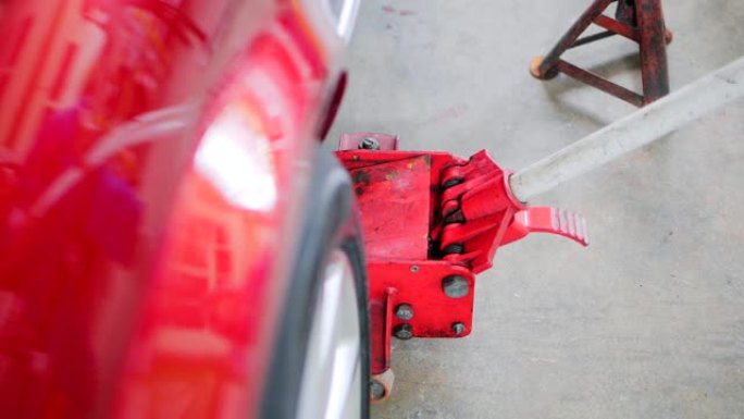 亚洲高级汽车修理工检查液压千斤顶提升红色轿车。汽车车库概念。4kslow motion镜头。发动机和