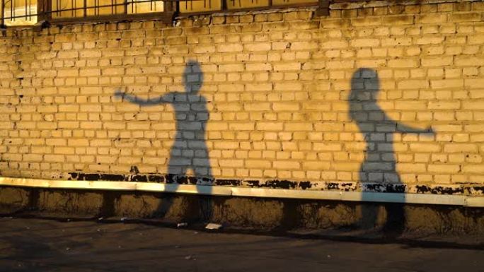 日落时，两个女性剪影在屋顶的砖墙上跳舞