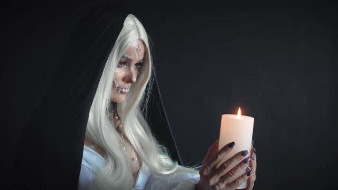 有着长长的白发和头上黑色兜帽的邪恶女巫手里拿着蜡烛