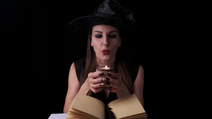 穿着黑色女巫服装和帽子的美丽性感女人，手里拿着蜡烛，让人联想。万圣节节日派对
