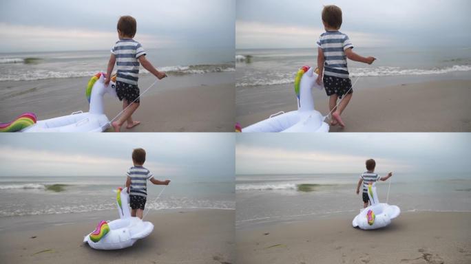 快乐的小男孩带着独角兽充气戒指在沙滩上奔跑