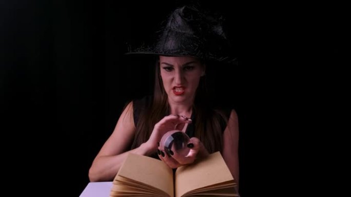 穿着黑色女巫服装和帽子的性感女人，手里拿着一个透明的魔球，让人联想。万圣节节日派对