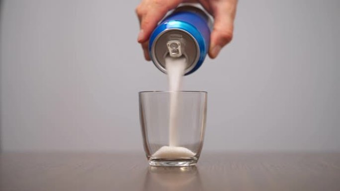 男子将糖从蓝色汽水罐倒入玻璃杯中。含糖饮料。孤立，在白色背景上